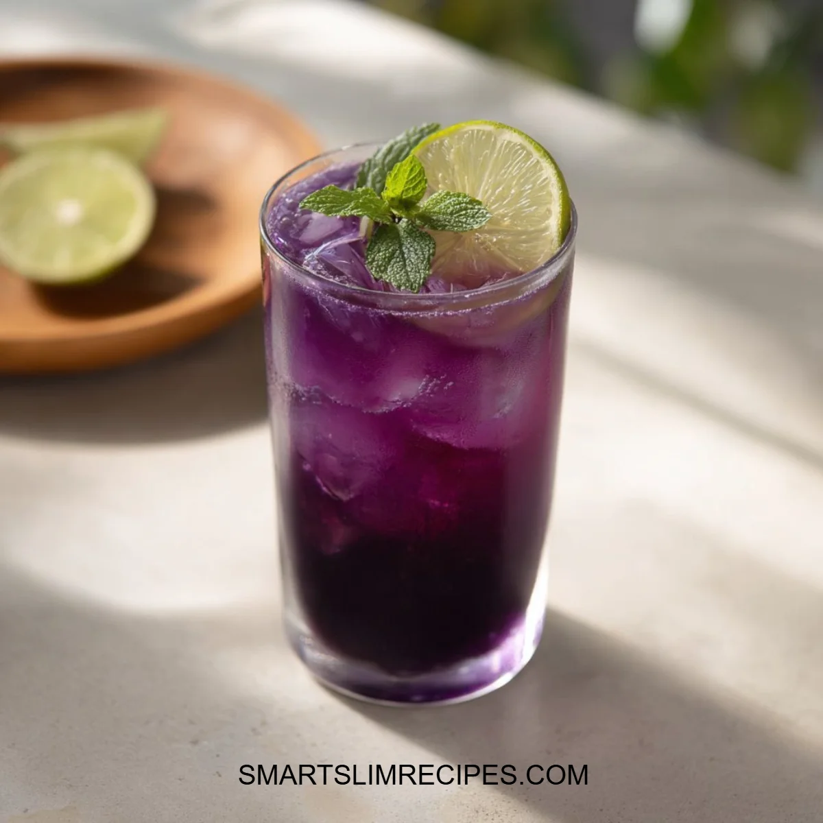 Glass of butterfly pea flower iced tea with lemon and mint garnish